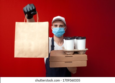 Young Food Delivery Man In A Protective Mask And Gloves Holds Boxes Of Food And Gives The Client, Quick Delivery Service During The Epidemic Of Coronavirus