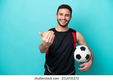 Young football player Brazilian man isolated on blue background inviting to come with hand. Happy that you came