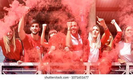 Young football supporter fans cheering with colored smoke watching soccer match together at stadium - Friends people group with red t-shirts having excited fun on sport world championship concept - Powered by Shutterstock