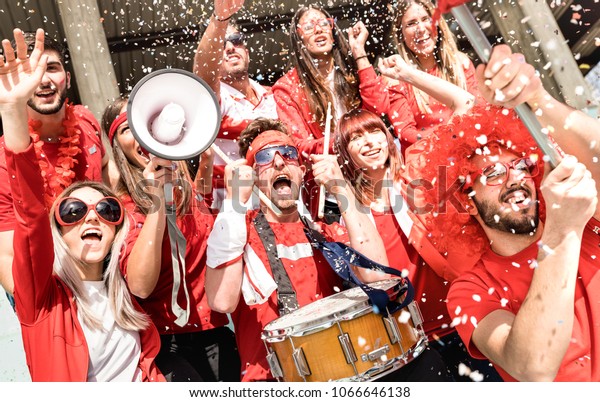 Young football supporter fans cheering with flag\
and confetti watching soccer match at stadium - Friends people\
group with red t-shirts having excited fun on sport world\
championship concept
