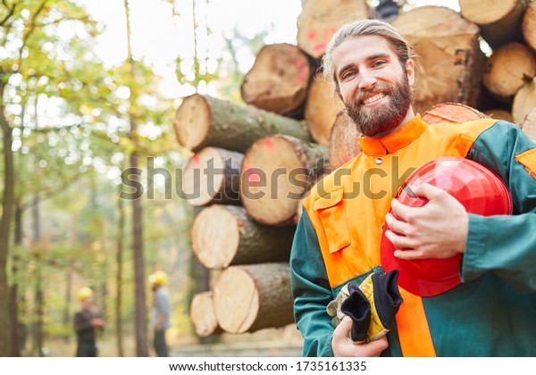 Young forest worker in protective\
clothing in front of a long wood cart at the wood\
harvest