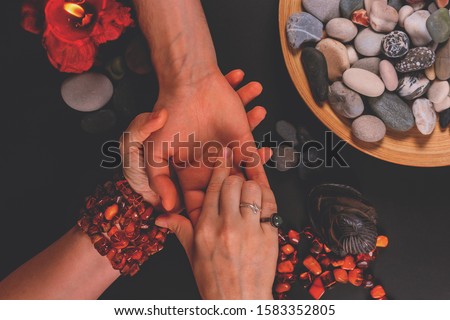 Young fortune teller divines the hand of young man around candles and other magical paraphernalia. Divine magic and occultism concept. Divination. Top view, toned.