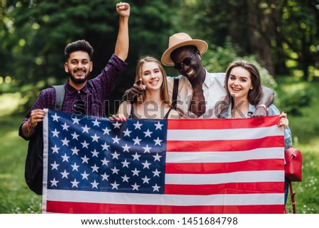 Young, four students relaxing on nature with american flag, celebrating 4th july - Independence Day. After education.