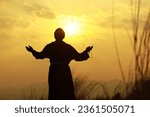 A young Franciscan friar with a rosary in hand standing on a hill top in the evening at the sunset. priest, monk, brother, praying on a hill top.