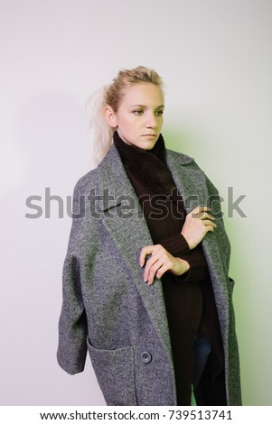 young freckled blonde girl posing in Studio on dark textured background. street style clothing: coat and white shirt. hair in a bun, healthy skin. emotional portrait