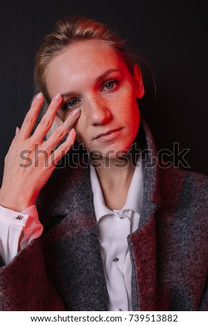 young freckled blonde girl posing in Studio on dark textured background. street style clothing: coat and white shirt. hair in a bun, healthy skin. emotional portrait