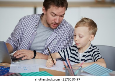 Young Freelance Father Interested In Sons Achievements Examining His Home Task While Using Laptop At Home