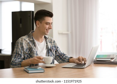 Young freelancer drinking coffee while using laptop at home