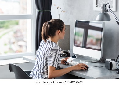 Young freelancer holding smartphone while using computer at home - Shutterstock ID 1834019761