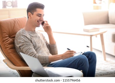 Young freelancer talking on phone while working at home