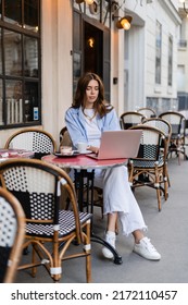 Young Freelancer Using Laptop Near Dessert And Coffee On Cafe Terrace In Paris