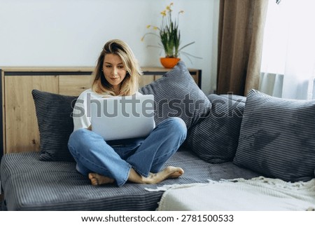 Young freelancer working remotely on laptop from home office while sitting on couch in apartment. High quality photo