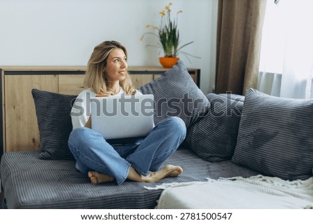 Young freelancer working remotely on laptop from home office while sitting on couch in apartment. High quality photo