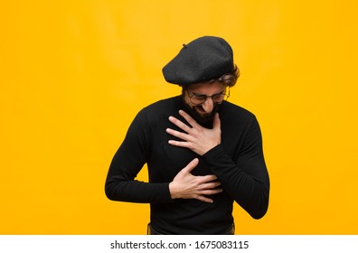 Young French Artist Man Laughing Out Loud At Some Hilarious Joke, Feeling Happy And Cheerful, Having Fun Against Orange Wall