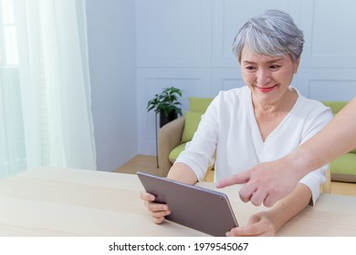 Young Friend Teaching Older Woman To Use Computer Tablet , Pointing At Screen, Elder Woman Asking Questions About Mobile Device. Elderly And Technology Concept.