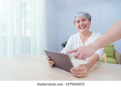 Young Friend Teaching Older Woman To Use Computer Tablet , Pointing At Screen, Elder Woman Asking Questions About Mobile Device. Elderly And Technology Concept.