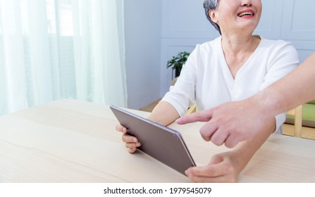 Young Friend Teaching Older Woman To Use Computer Tablet , Pointing At Screen, Elder Woman Asking Questions About Mobile Device. Elderly And Technology Concept.