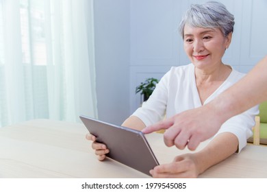 Young Friend Teaching Older Woman To Use Computer Tablet , Pointing At Screen, Elder Woman Asking Questions About Mobile Device. Elderly And Technology Concept.