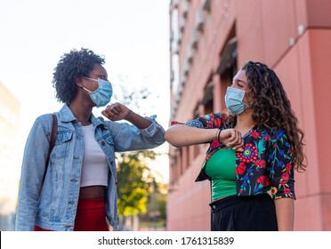 Junge und freundliches afrikanisches Mädchen und kaukasisches Mädchen, das soziale Distanz hält, sich gegenseitig grüßen, indem sie sich mit Ellenbogen anstatt mit Umarmungen, Küssen oder Handshaking, mit Maske zur Vorbeugung gegen eine Infektion mit dem Koronavirus,