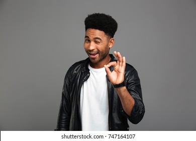 Young friendly african guy winks one eye while showing OK gesture, isolated on gray background - Shutterstock ID 747164107