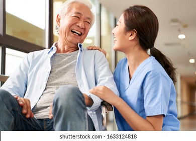 young friendly asian female caregiver talking chatting to happy senior man in hallway of nursing home