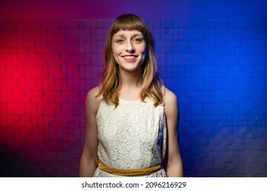 A Young Friendly Cute Girl With Brown Hair, Bangs In A White Dress Looks Into The Camera And Smiles On A Colored Background. The Concept Of Natural Female Beauty