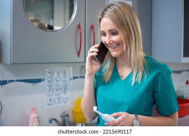 Young Friendly Dentist Standing In Office While Talking On Phone With Patient And Holding Tooth Brush In Hand.