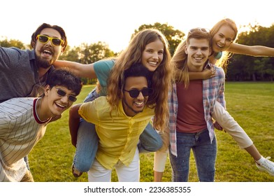 Young friendly multiracial people from high school, friends relaxing in summer park and giving each other ride on their backs having fun posing for lifestyle shot, located at green lawn - Shutterstock ID 2236385355