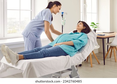 Young friendly nurse help pregnant woman in receiving IV drip infusion and vitamin therapy in medical clinic. Gynecologist doctor giving consultation to her expectant patient lying on the couch. - Powered by Shutterstock