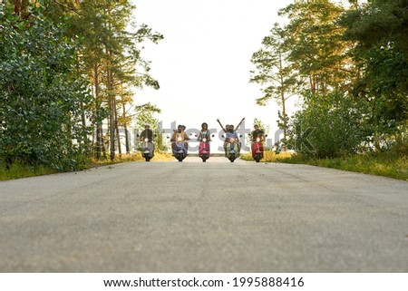 Young friendly people driving colorful scooters in row along asphalt road in sunny nature. Leisure, fun and entertainment concept