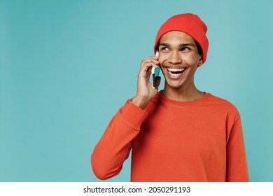 Young friendly smiling happy african american man in orange shirt hat talk speak on mobile cell phone conducting pleasant conversation isolated on plain pastel light blue background studio portrait. - Shutterstock ID 2050291193
