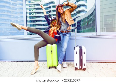 Young friends girls going crazy about their new trip, screaming laughing and having fun near airport with their bright luggage, enjoy travel together. Positive playful emotions, urban background.