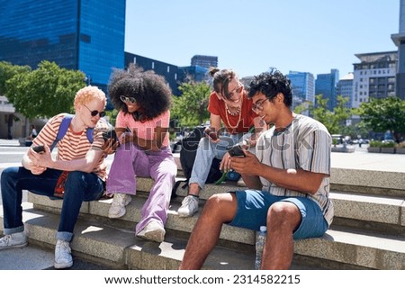 Young friends hanging out and talking, using smart phones together in sunny city park