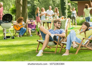 Young friends having barbecue picnic in the nature, playing guitar, playing badminton, enjoying sunny summer day outdoor