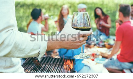 Young friends having barbecue picnic in nature - Group of people camping, drinking wine and making bbq dinner outdoor - Focus on hand glass - Youth and friendship concept - Vintage camera filter