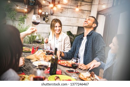 Young Friends Having Fun Drinking Red Wine On Balcony At House Dinner Pic Nic Party - Hipster Millennial People Eating Bbq Food At Fancy Restaurant Together - Dinning Life Style Concept On Warm Filter