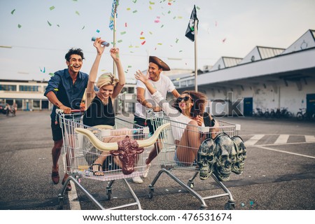 Young friends having fun on shopping trolleys. Multiethnic young people racing on shopping cart.