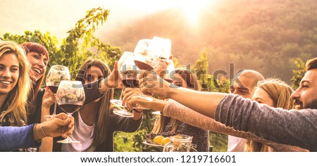 Young friends having fun outdoor - Happy people enjoying harvest time together at farm house winery countryside - Youth friendship concept - Hand toasting red wine at pic nic in vineyard before sunset