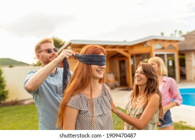 Young Friends Having Fun At Poolside Summertime Outdoor Party, Playing Blind Man's Buff, Guy Placing Blindfold Over Girl's Eyes