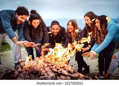 Young friends having fun together at night party around bonfire - Friendship life style concept with happy people traveler making themselves warm by campfire at dusk time - Vivid contrast filter - Powered by Shutterstock