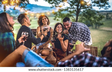 Young friends having fun at vineyard after sunset - Happy people millennial camping at open air pic nic under bulb lights - Youth friendship concept with guys and girls drinking wine at barbeque party