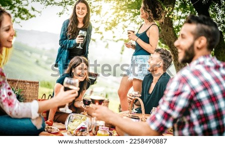 Young friends having fun at vineyard place during sunset - Food and beverage concept with guys and girls drinking wine at barbeque party - Happy people camping at open air pic nic on warm vivid filter
