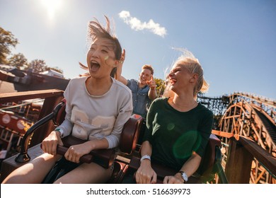 Young friends on thrilling roller coaster ride. Young women and men having fun at amusement park. - Shutterstock ID 516639973