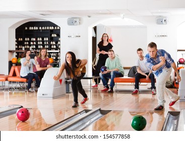 Young friends playing in bowling alley with people in background