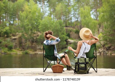 Young Friends Resting On Pier Near Lake. Camping Season