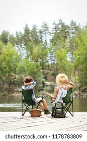 Young Friends Resting On Pier Near Lake. Camping Season