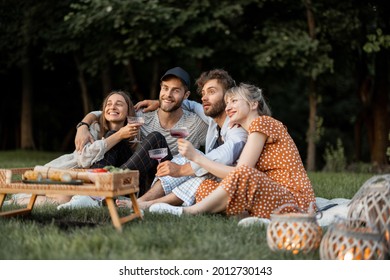 Young friends sitting together by the barbeque, talking and drinking wine in a close and friendly atmosphere, having a picnic in the evening - Powered by Shutterstock