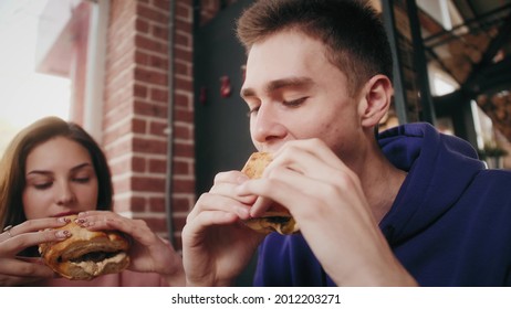 Young Friends Students Eating Unhealthy Food Or Veggie Burgers Enjoying Dinner, Eating In The Grill Burger Cafe.