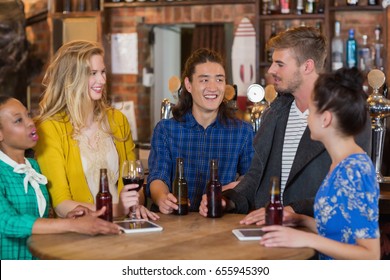 Young friends talking while standing by digital tablets and beer bottles on table in pub