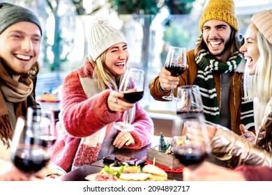 Young friends toasting red wine at restaurant patio - Happy people having fun together at winery bar wearing winter clothes - Dinning life style concept on bright filter with focus on left woman